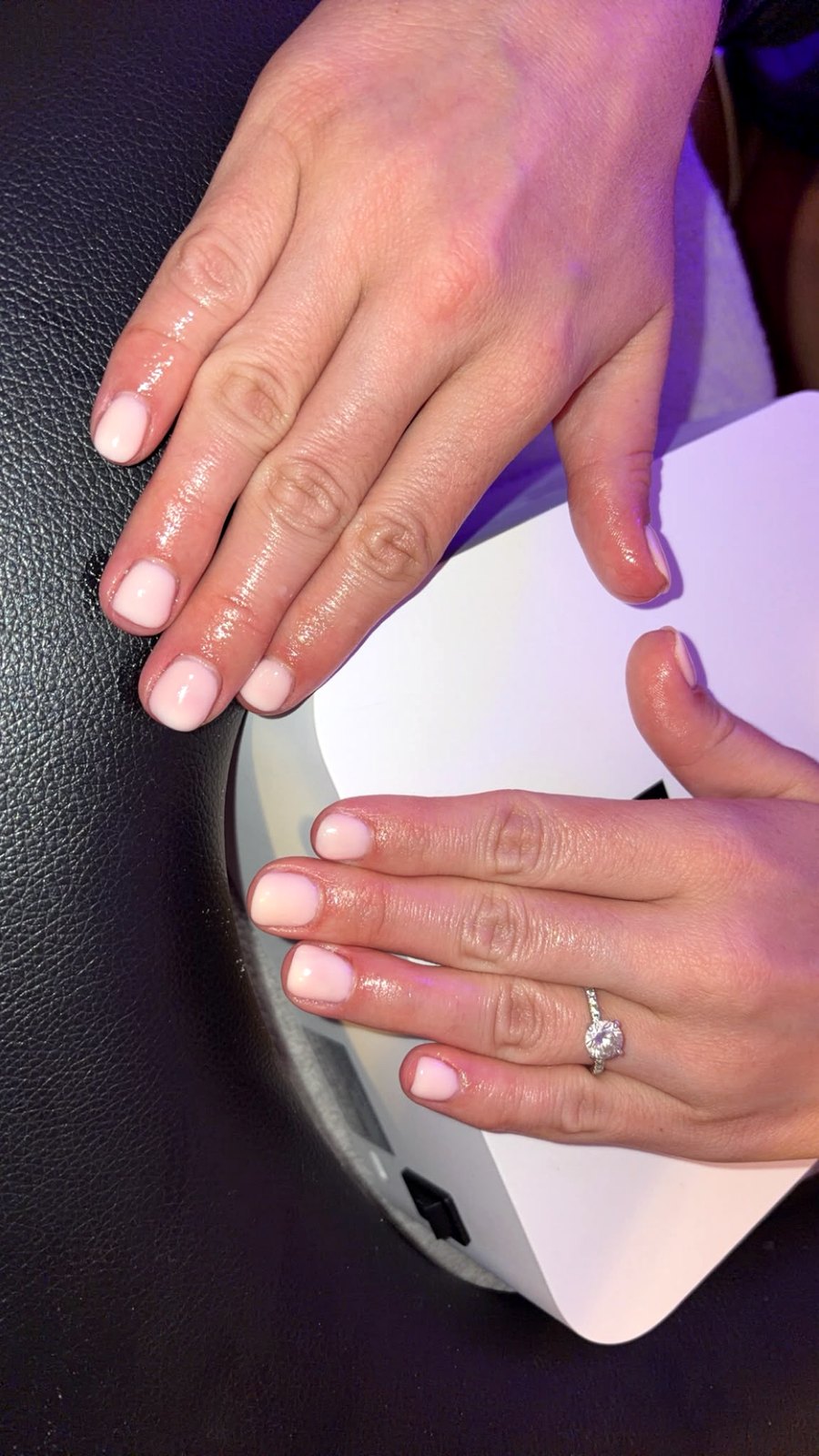 Glossy nude nails curing under the lamp